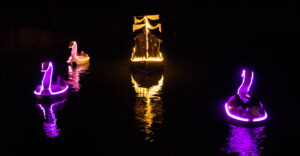 Illuminated miniature ship floating on water at night.